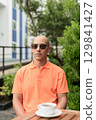 Bald Hispanic man face sitting outdoors at cafe restaurant wearing orange polo shirt 129841427