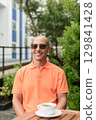 Bald Hispanic man face sitting outdoors at cafe restaurant wearing orange polo shirt 129841428