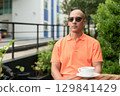 Bald Hispanic man face sitting outdoors at cafe restaurant wearing orange polo shirt 129841429