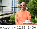 Bald Hispanic man face sitting outdoors at cafe restaurant wearing orange polo shirt 129841430
