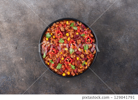 Chili con carne with fresh herbs and nachos chips on a gray background. Top view. Mexican cuisine. Chili con carne with fresh herbs and nachos chips on a gray background. Top view. Mexican cuisine. 129841791