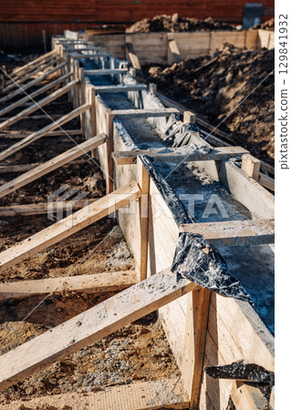 Wooden formwork is supporting strip foundation made of concrete, reinforcement and waterproofing Wooden formwork is supporting strip foundation made of concrete, reinforcement and waterproofing 129841932