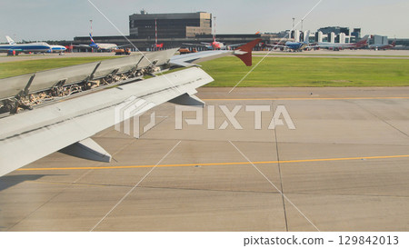 Airplane wing over airport runway during landing with deployed flaps and spoilers 129842013