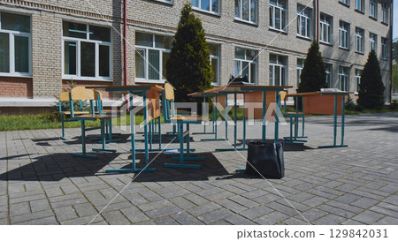 Deserted school desks and chairs lined up outside school building with books and bag on the ground during the school day 129842031