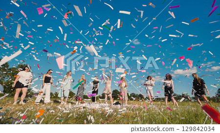 Friends jubilantly celebrating graduation with a confetti toss in a colorful meadow under a clear blue sky 129842034
