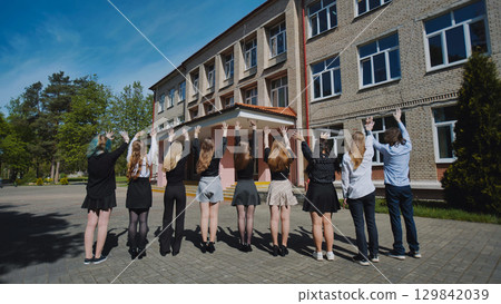 Group of happy students waving goodbye to their school on the last day, celebrating the end of the academic year 129842039