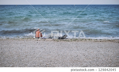 Senior man relaxing on Crimean beach with dog watching the waves 129842045