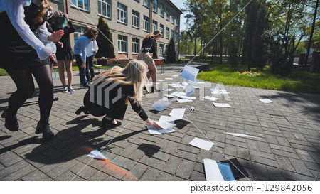 Students joyfully celebrating the end of their exams by throwing papers in the air and enjoying freedom in the schoolyard Students joyfully celebrating the end of their exams by throwing papers in the air and enjoying freedom in the schoolyard 129842056