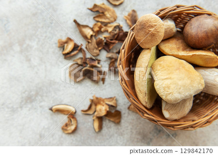 Fresh mushrooms overflowing from wicker basket onto table with dried mushrooms Fresh mushrooms overflowing from wicker basket onto table with dried mushrooms 129842170