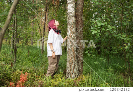 Young girl with pink hair exploring forest and touching tree trunk Young girl with pink hair exploring forest and touching tree trunk 129842182