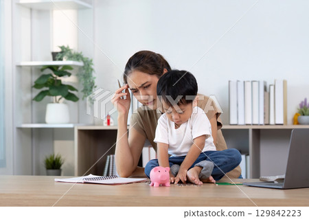 Financial Stress. Parent looking worried while child plays with piggy bank. 129842223
