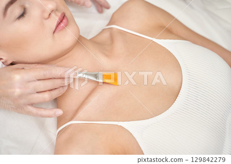 Female getting skincare cosmetic treatment with brush on chest in spa setting 129842279