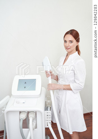 Caucasian female adult beautician operating modern aesthetic device in clinical 129842283