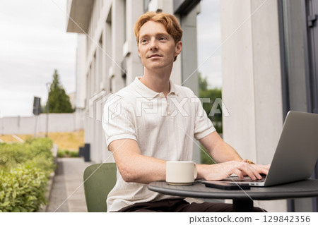 Young freelancer working on laptop sitting in street cafe using internet Young freelancer working on laptop sitting in street cafe using internet 129842356