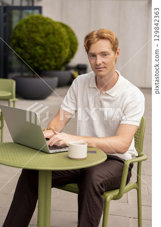 Smiling digital nomad browsing online writing notes on computer at cafe table Smiling digital nomad browsing online writing notes on computer at cafe table 129842363