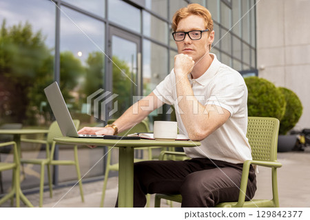 Redhead businessman generating ideas holding chin while doing his remote job Redhead businessman generating ideas holding chin while doing his remote job 129842377