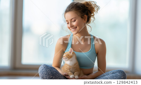 Smiling woman in sportswear cuddling a cute orange kitten indoors 129842413