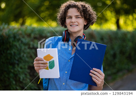 Curly-haired teen with a book in hands in the park 129843194