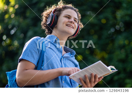 Curly-haired teen with a book in hands in the park 129843196