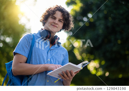 Curly-haired teen with a book in hands in the park 129843198