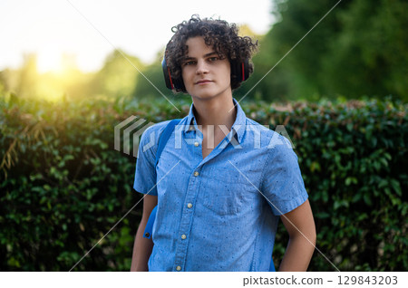 Curly-haired teen in blue shirt near the bush in the park 129843203