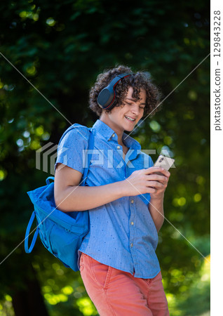 Curly-haired teen in blue shirt in the park looking contented 129843228