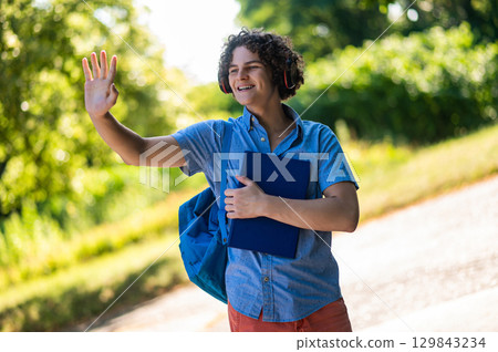 Teen in blue thsirt in the park with headphones and books in hands 129843234