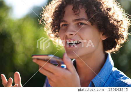 Curly-haired teen with a phone in hands in the park 129843245
