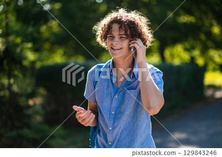 Curly-haired teen with a phone in hands in the park 129843246