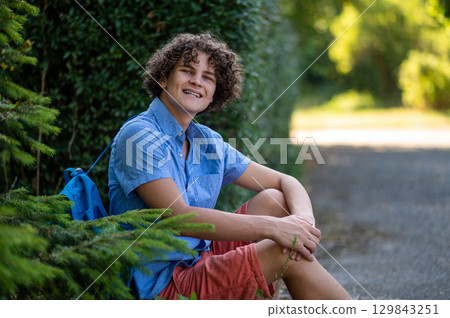 Curly-haired teen in blue tshirt spending time in the park 129843251