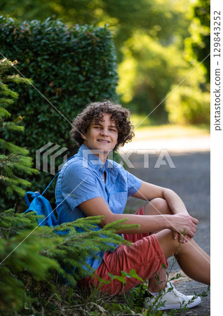 Curly-haired teen in blue tshirt spending time in the park 129843252