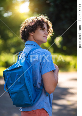 Curly-haired teen in blue tshirt spending time in the park 129843253