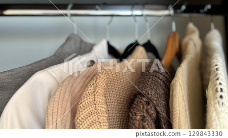 Neatly hung womens wardrobe on hangers in closet, organized autumn and winter fashion, warm knitted sweaters, seasonal clothing minimalistic organization, stylish clothes storage, womens fashion 129843330