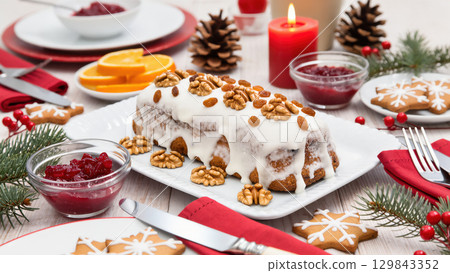 Christmas festive table with nut cake topped with icing and walnuts, surrounded by cookies, berries, candles, and cranberry sauce 129843352