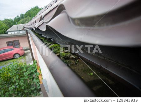 Dirty gutter under the roof clogged with moss and debris Dirty gutter under the roof clogged with moss and debris 129843939