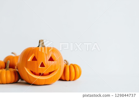 A cheerful Halloween Pumpkin surrounded by little Mini Pumpkins on a clean White Background 129844737