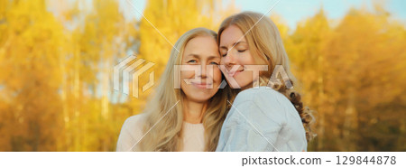 Happy two women, smiling mature mother and adult daughter hugging in autumn park Happy two women, smiling mature mother and adult daughter hugging in autumn park 129844878