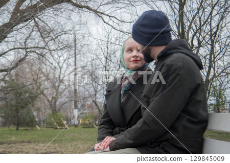 Young woman and man sitting on a bench. Boyfriend and girlfriend outdoors. Happy couple Young woman and man sitting on a bench. Boyfriend and girlfriend outdoors. Happy couple 129845009