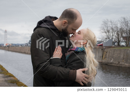 Pretty young woman with long blonde hair and man couple hugging each other kissing at seaside Pretty young woman with long blonde hair and man couple hugging each other kissing at seaside 129845011