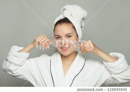 Healthy young woman with moisturizing, rejuvenating white fabric sheet mask from her face Healthy young woman with moisturizing, rejuvenating white fabric sheet mask from her face 129845048