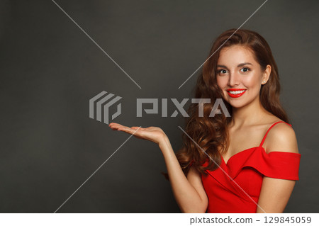 Smiling woman holding empty open palm hand and looking at camera on black background Smiling woman holding empty open palm hand and looking at camera on black background 129845059
