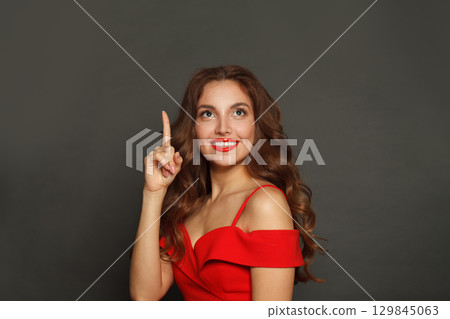 Pretty young model woman pointing finger up while standing on black background Pretty young model woman pointing finger up while standing on black background 129845063