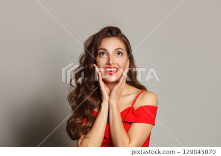 Nice surprised woman with curly hairstyle and makeup holding her hand with her face Nice surprised woman with curly hairstyle and makeup holding her hand with her face 129845070