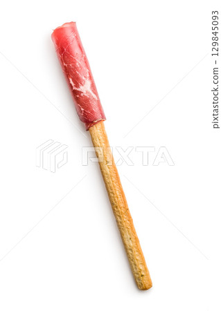 Slices of smoked bresaola and grissini sticks isolated on white background. 129845093