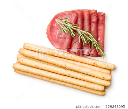 Slices of smoked bresaola and grissini sticks isolated on white background. 129845095