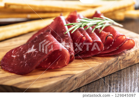 Slices of smoked bresaola on cutting board on wooden table. 129845097