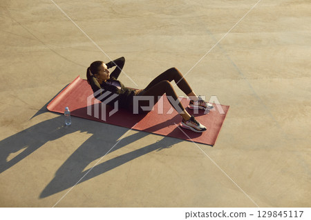Sporty young woman in black sportswear doing sport exercises shaking press outdoors. Sporty young woman in black sportswear doing sport exercises shaking press outdoors. 129845117