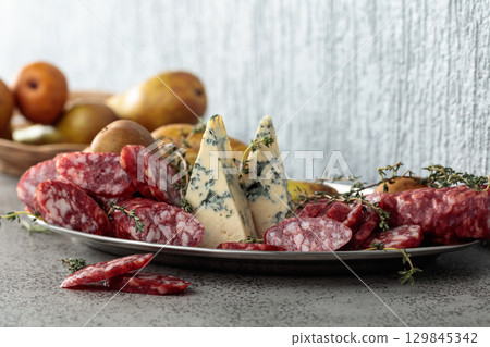 Blue cheese, dry-cured sausages, thyme and pears on a stone table. Blue cheese, dry-cured sausages, thyme and pears on a stone table. 129845342