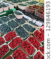 Punnets of ripe raspberries, blueberries, and cherries are neatly arranged on a market stall, creating a vibrant display of colorful fresh produce 129846193