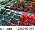 Cardboard and plastic containers overflowing with ripe blueberries, raspberries, and cherries create a vibrant display at a local farmers market, celebrating the abundance of summer fruits 129846195